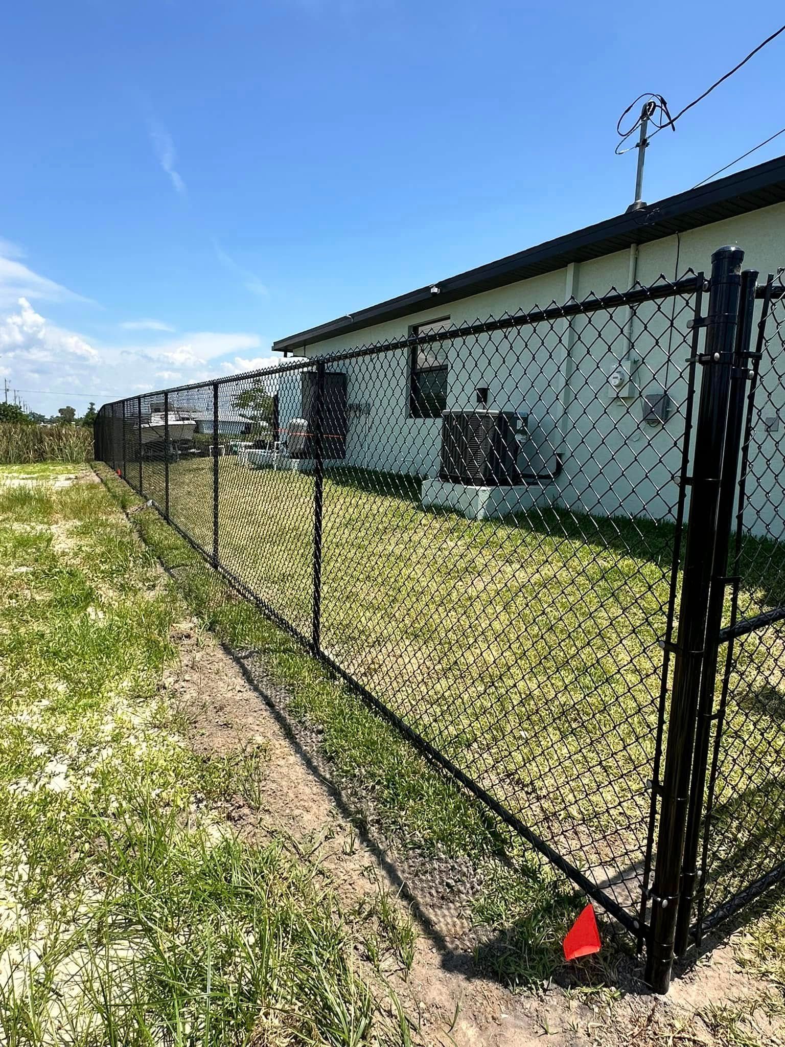 Black chain-link fence surrounding a white building with a blue sky overhead.