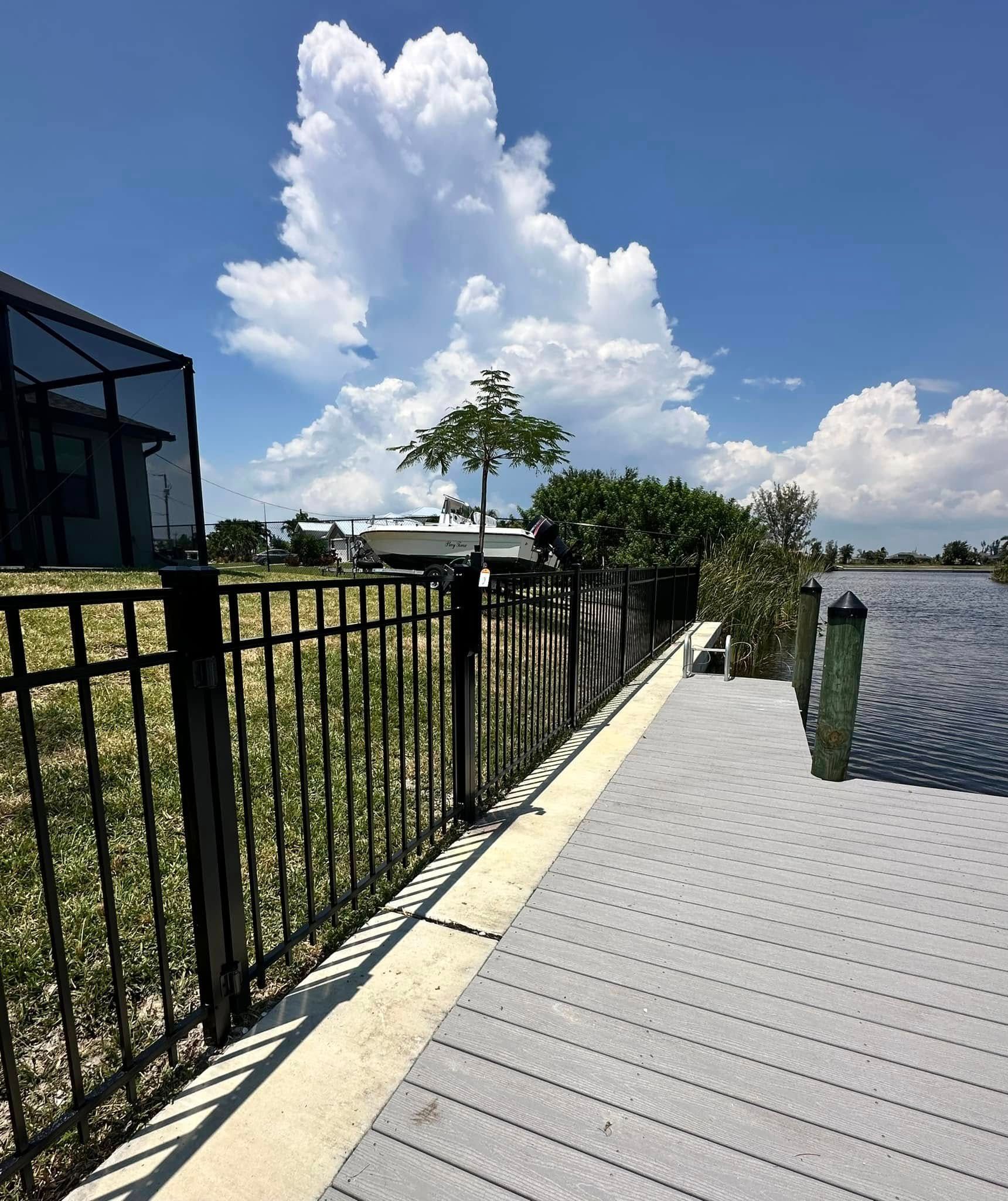 Dock and fence along a waterway, with a house on the left and a large cloud in the sky.