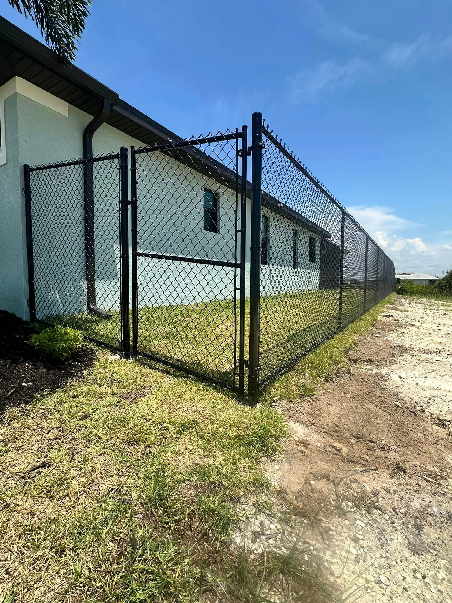 Black fence encloses a yard next to a light blue building under a bright blue sky.