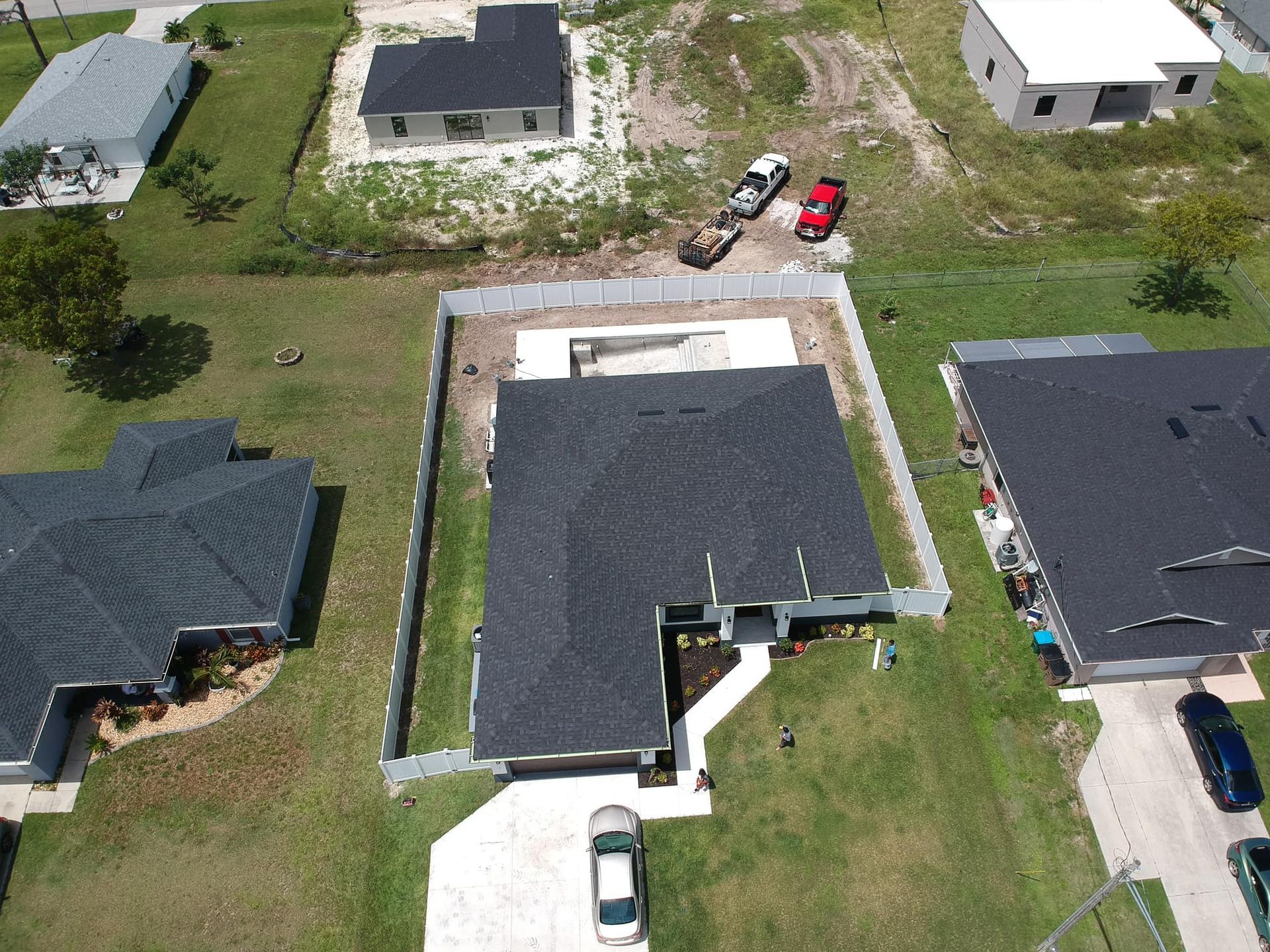 Aerial view of a residential neighborhood. A newly built house with a dark roof and car parked in the driveway.