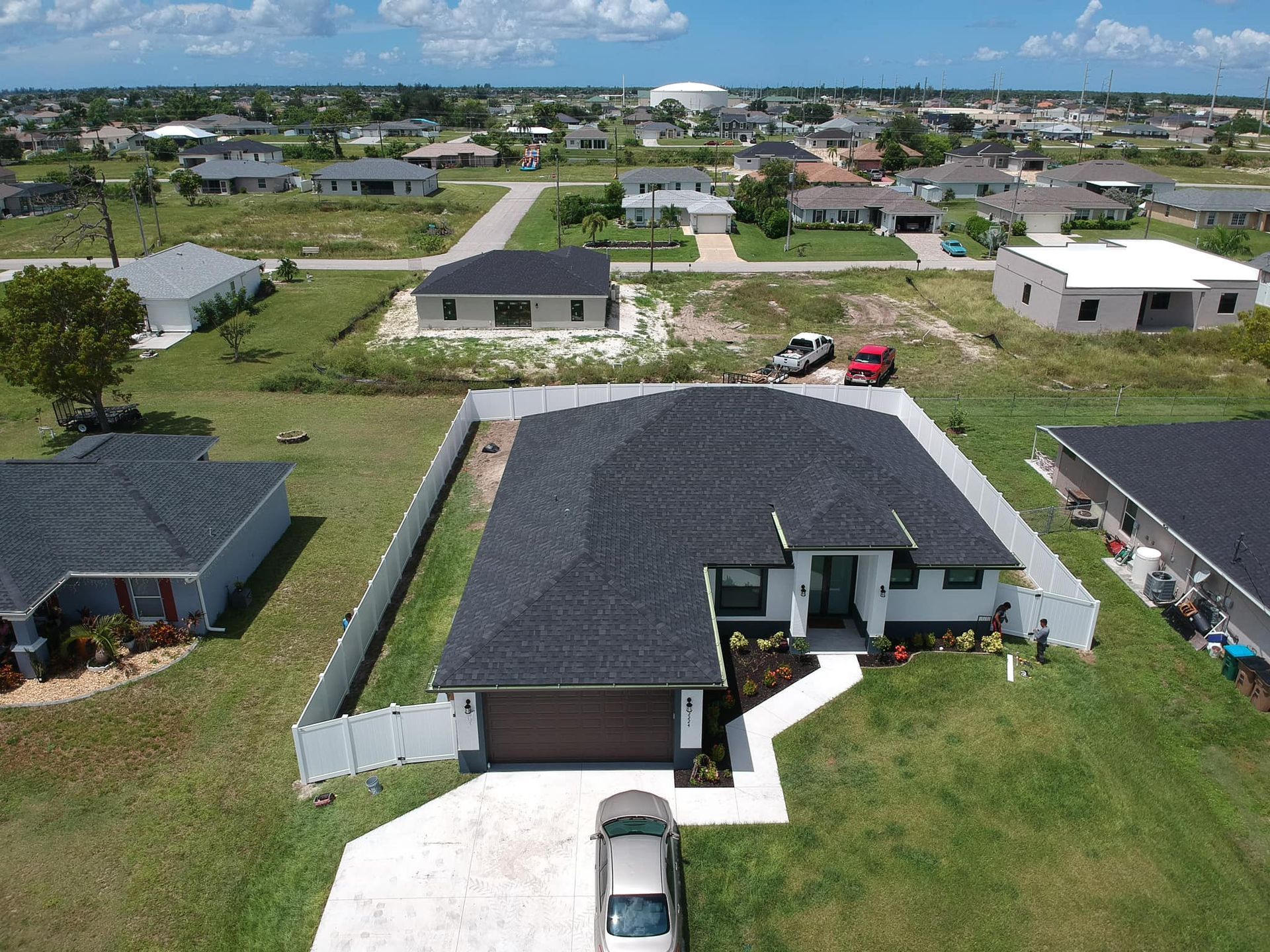 Aerial view of a modern, single-story house with a dark roof and white exterior in a suburban neighborhood.