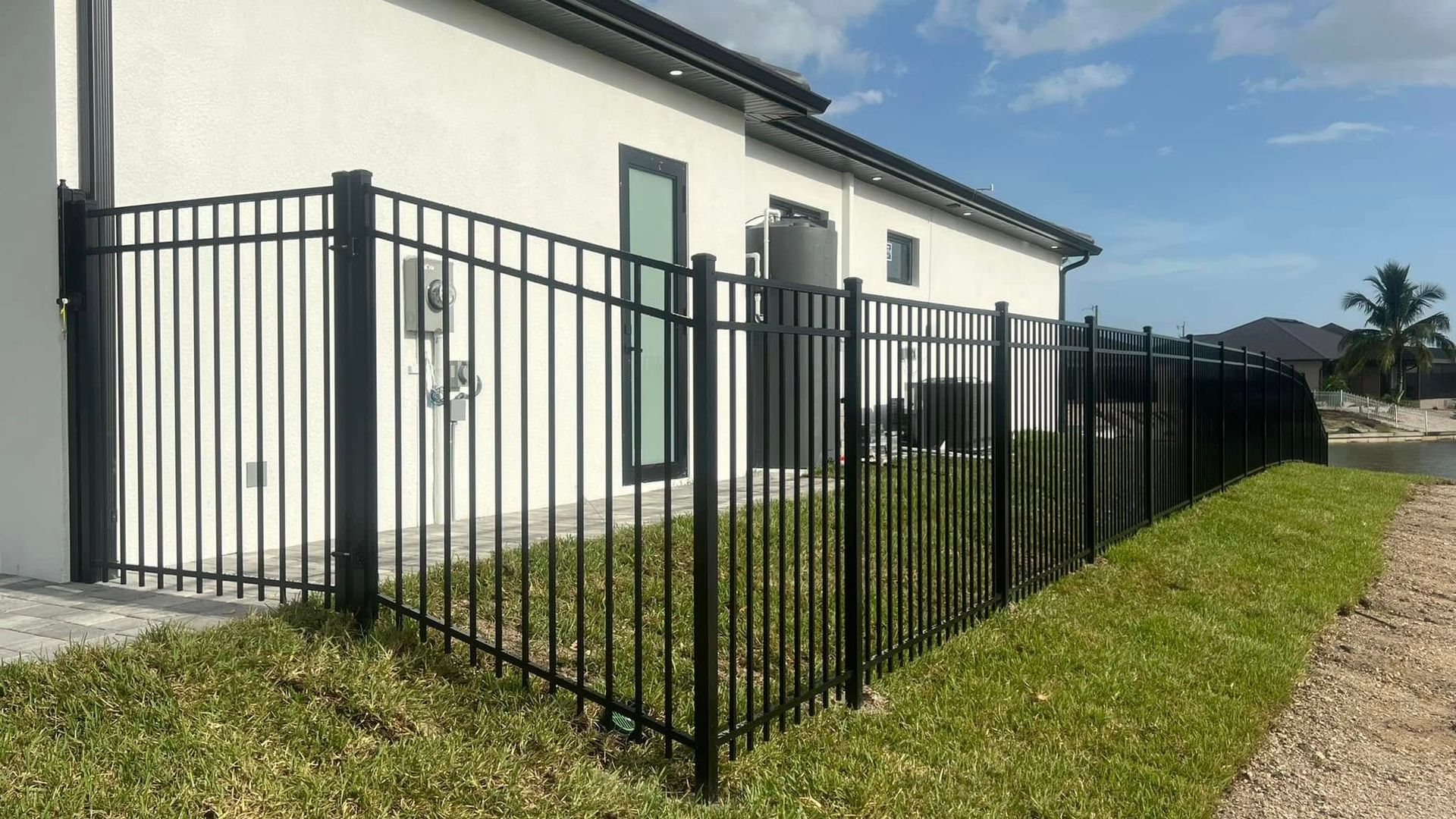 Black metal fence bordering a house with a white exterior and green grass.
