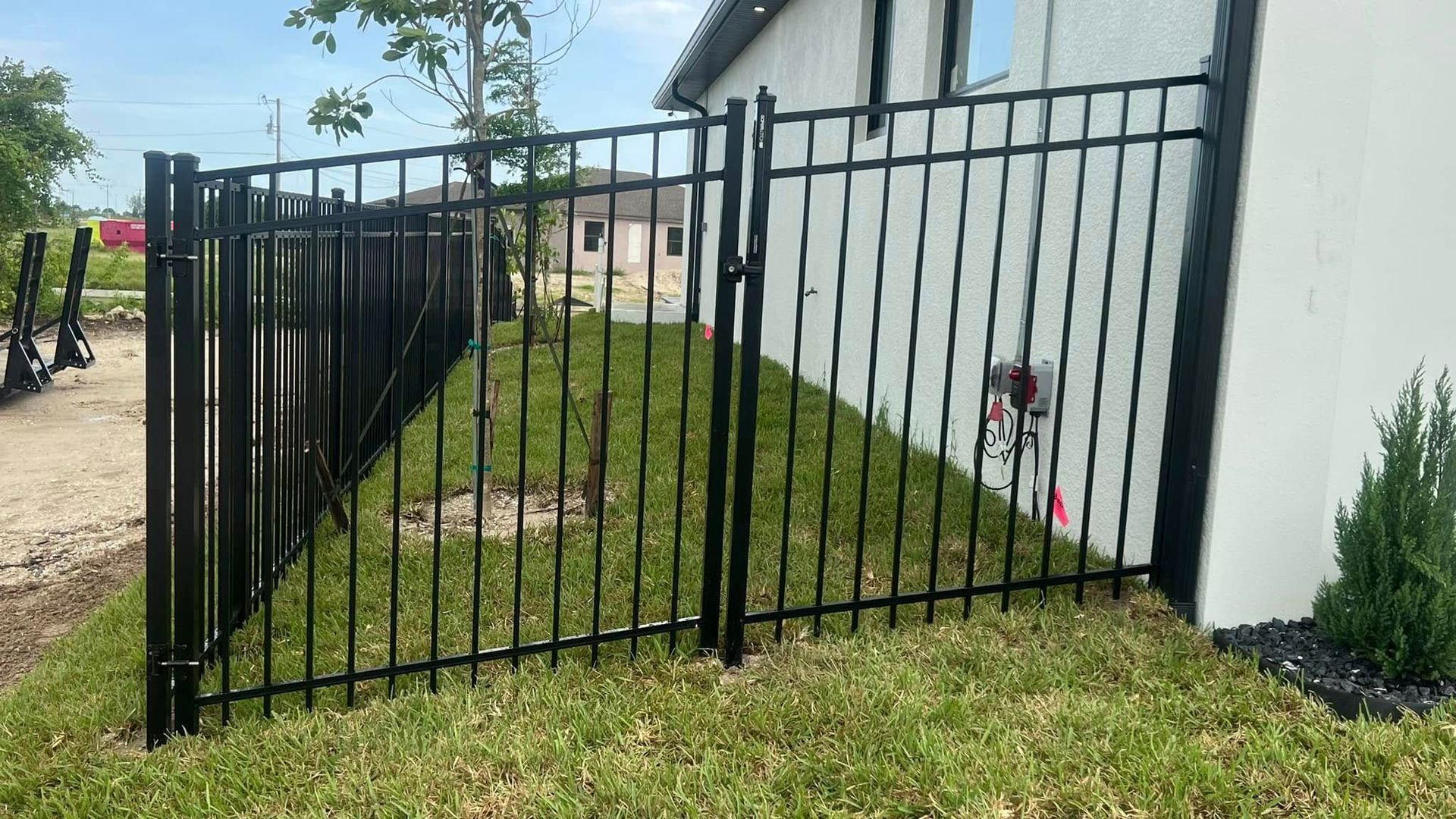 Black metal fence surrounding a grassy yard next to a white house.