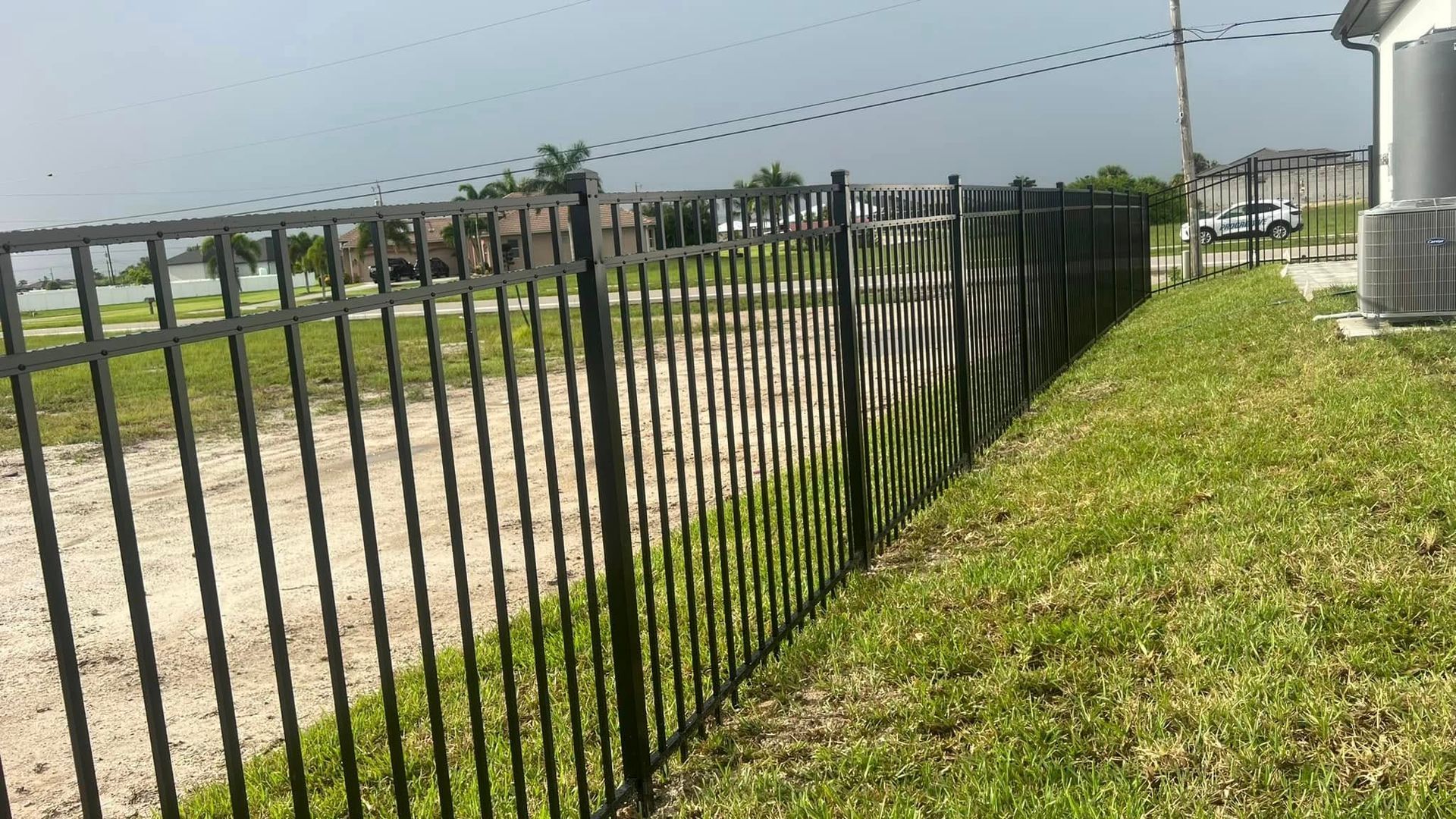 Black metal fence bordering a grassy yard next to a gravel path, a cloudy day.