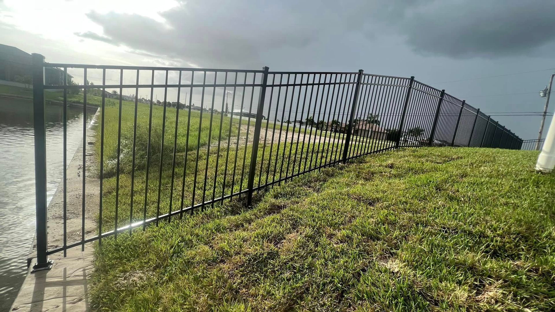 Black metal fence along grassy bank, overcast sky.
