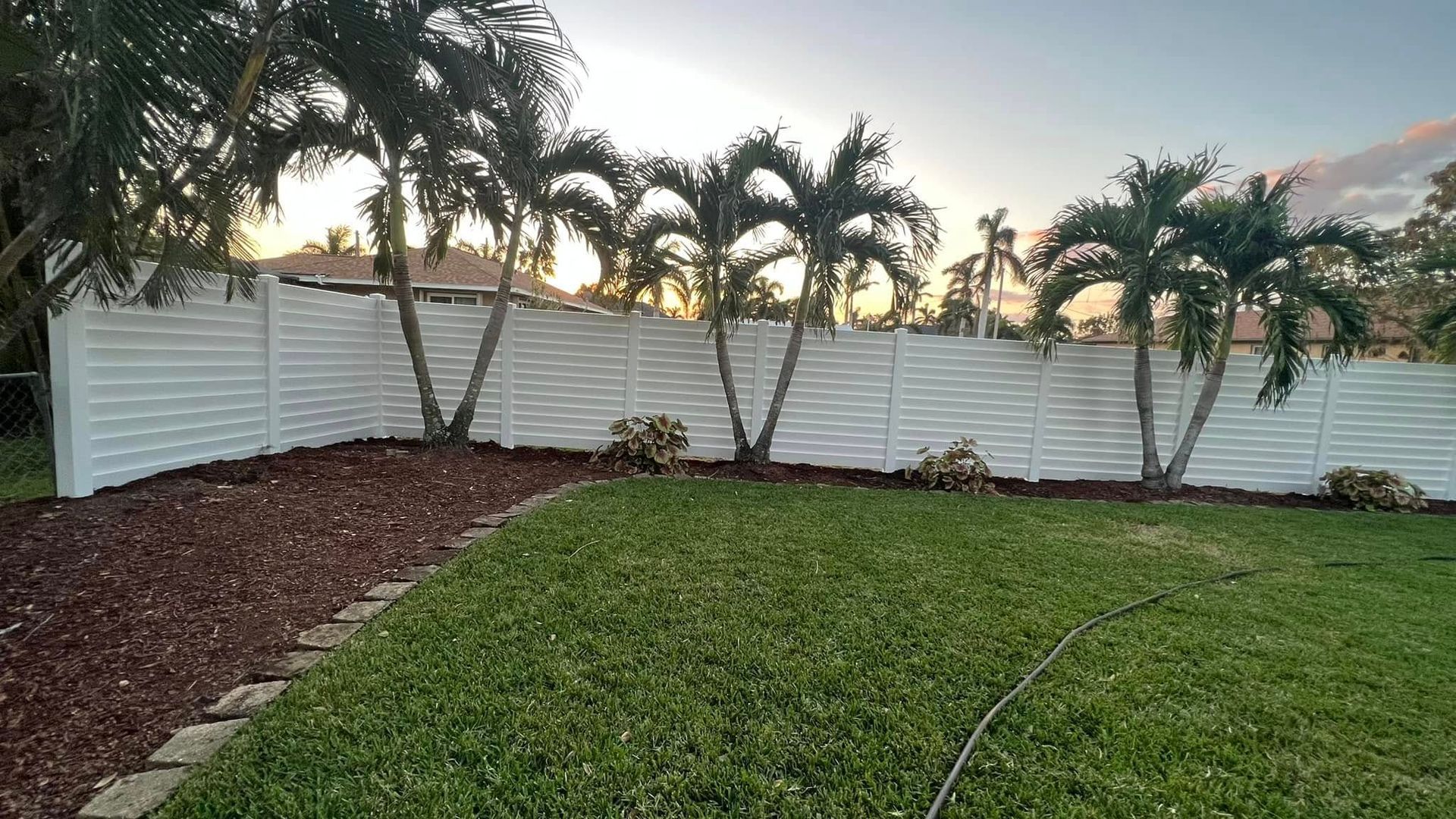 White privacy fence with palm trees and a green lawn.