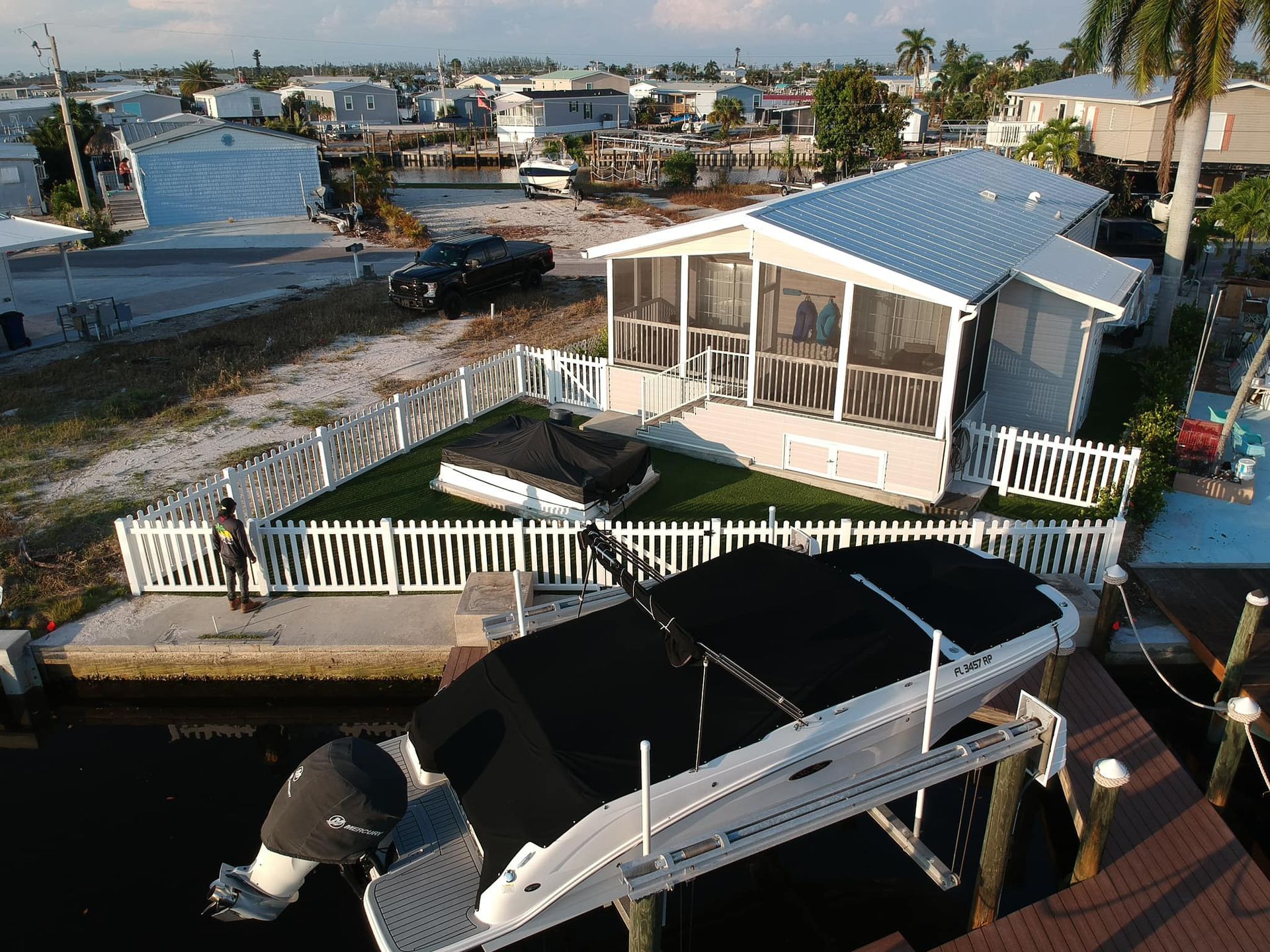 A boat docked next to a house with a white fence in a waterfront neighborhood.