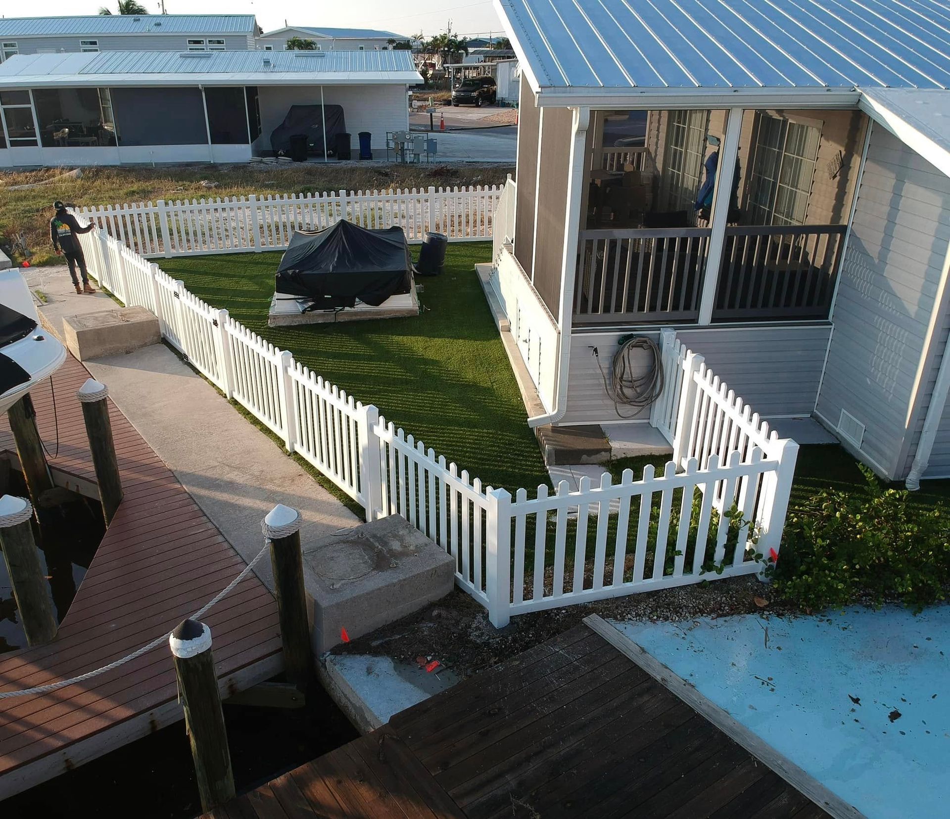 White picket fence surrounds a grassy yard next to a house and a dock with a boat in the Florida Keys.