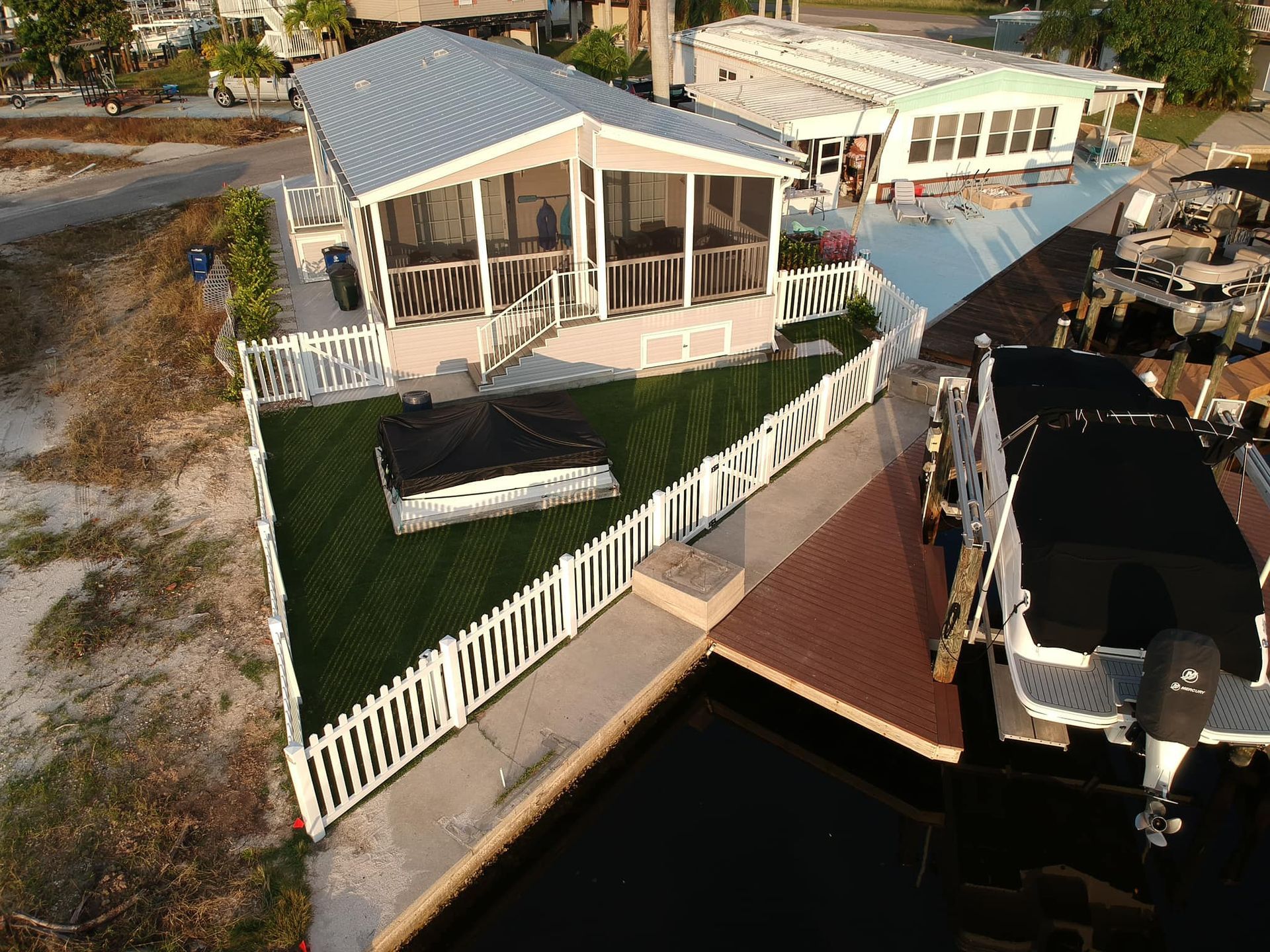 House with screened porch and white picket fence next to dock with boats.
