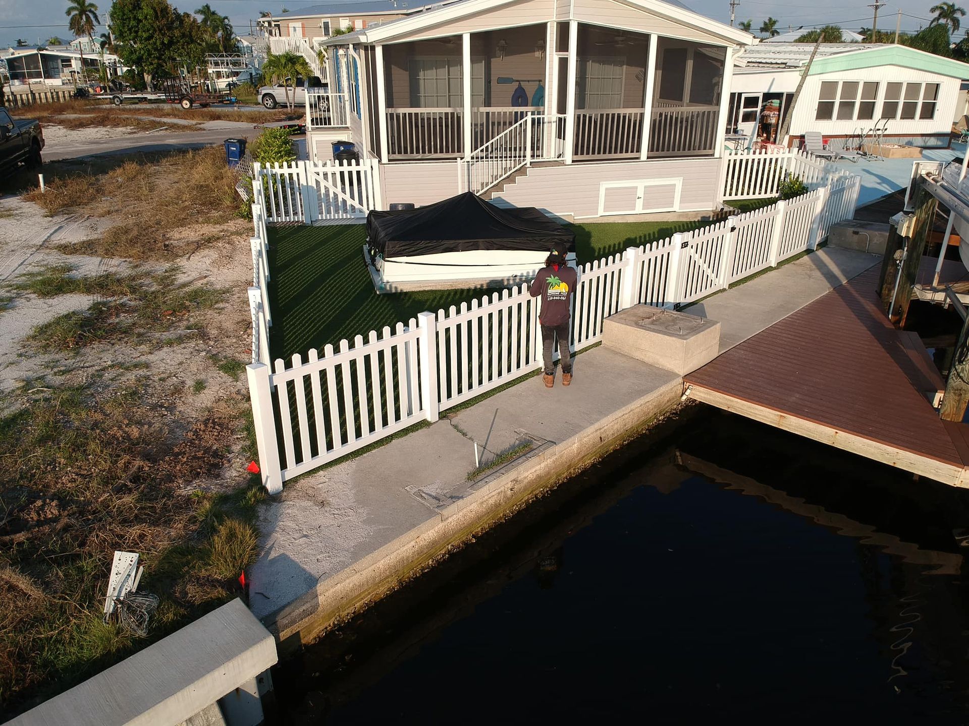 A person near a white picket fence and a house by a waterway.