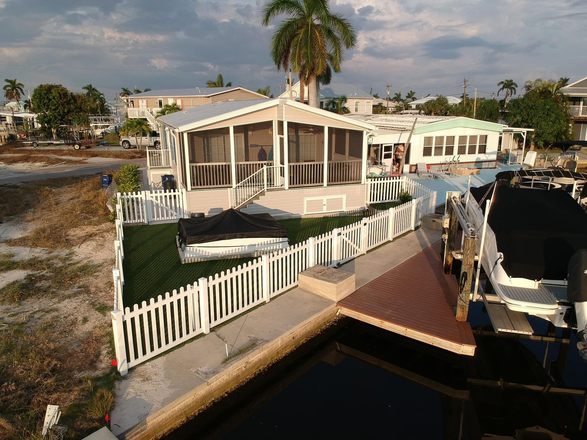 House with screened porch, white picket fence by the water, boat dock, palm tree.