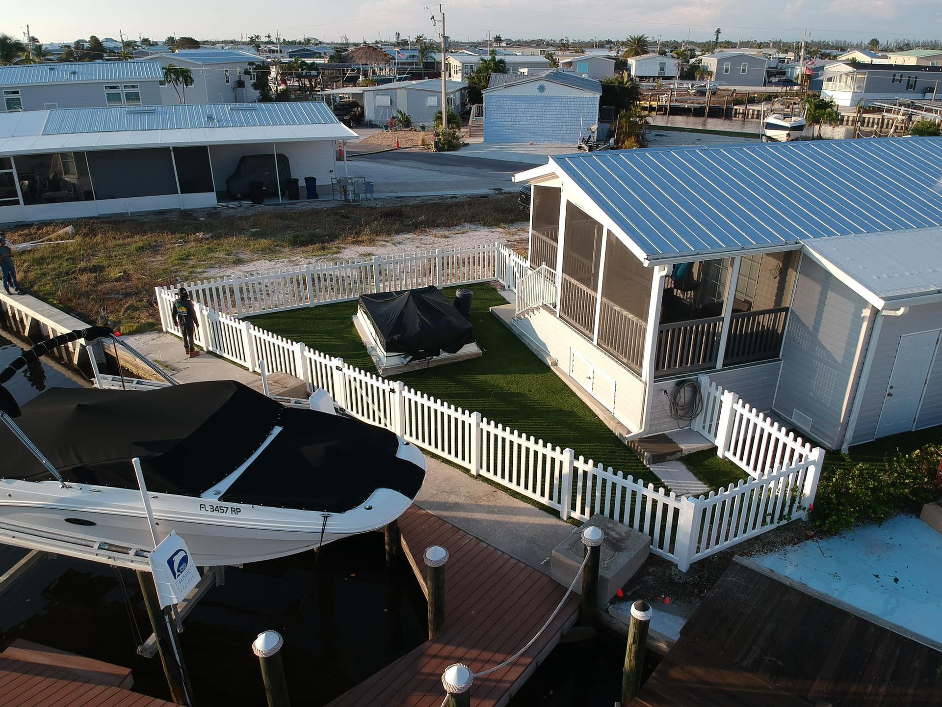 An aerial view of white homes with boats docked in front, a man walks on a dock.