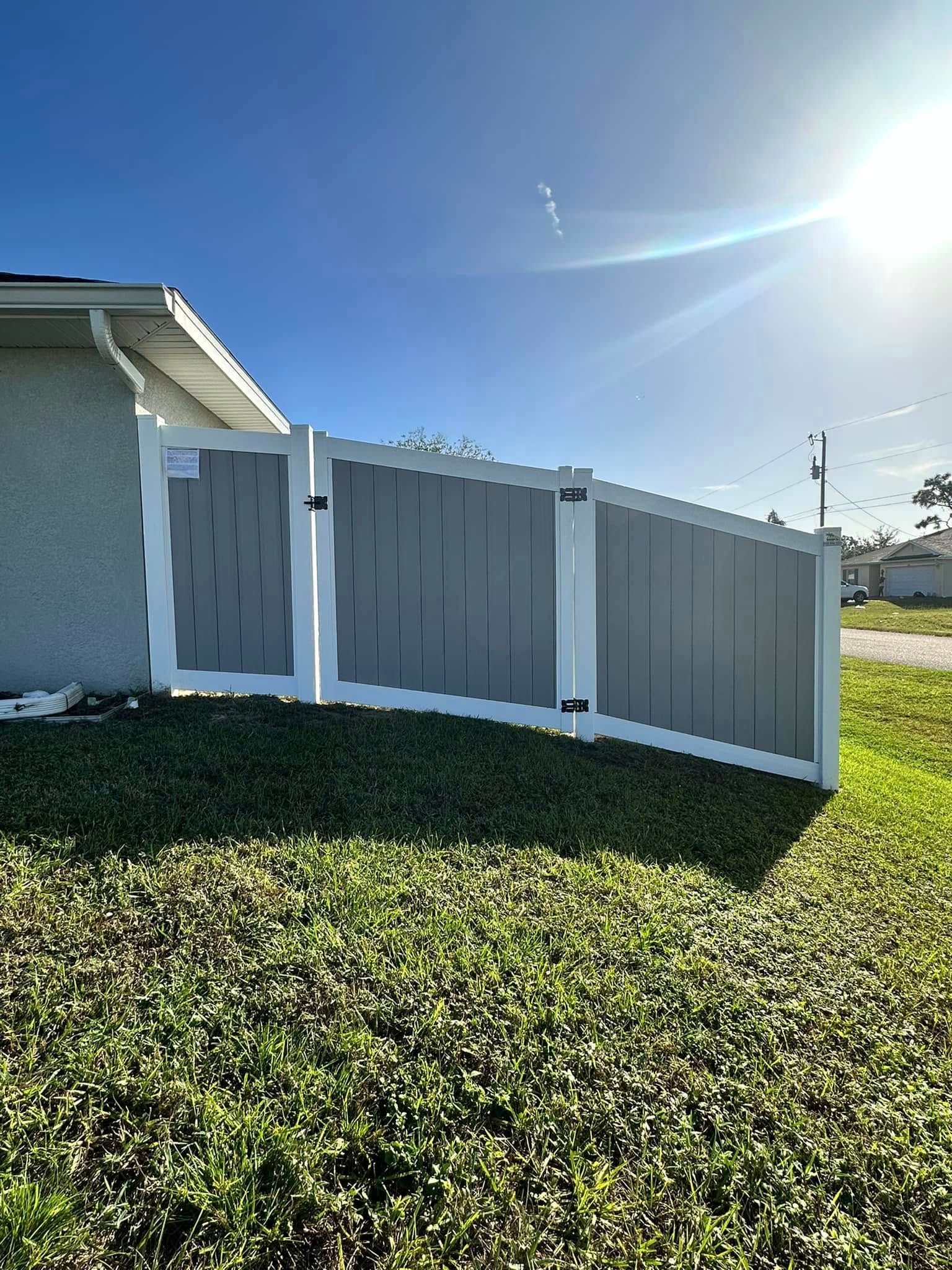 Gray and white fence with gate in front of a house on a sunny day.