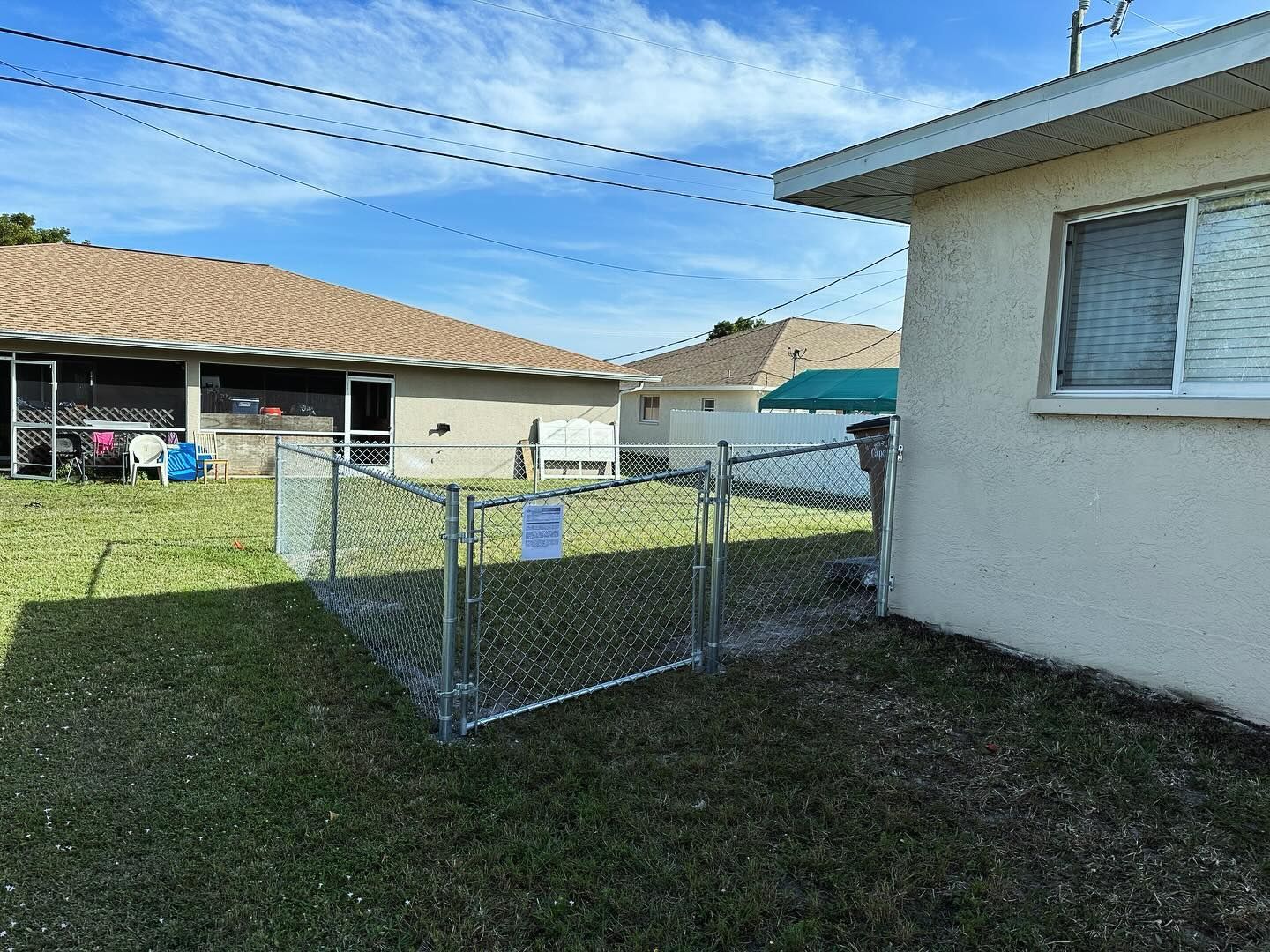 Chain-link fence enclosure in grassy yard next to a building, under a blue sky.