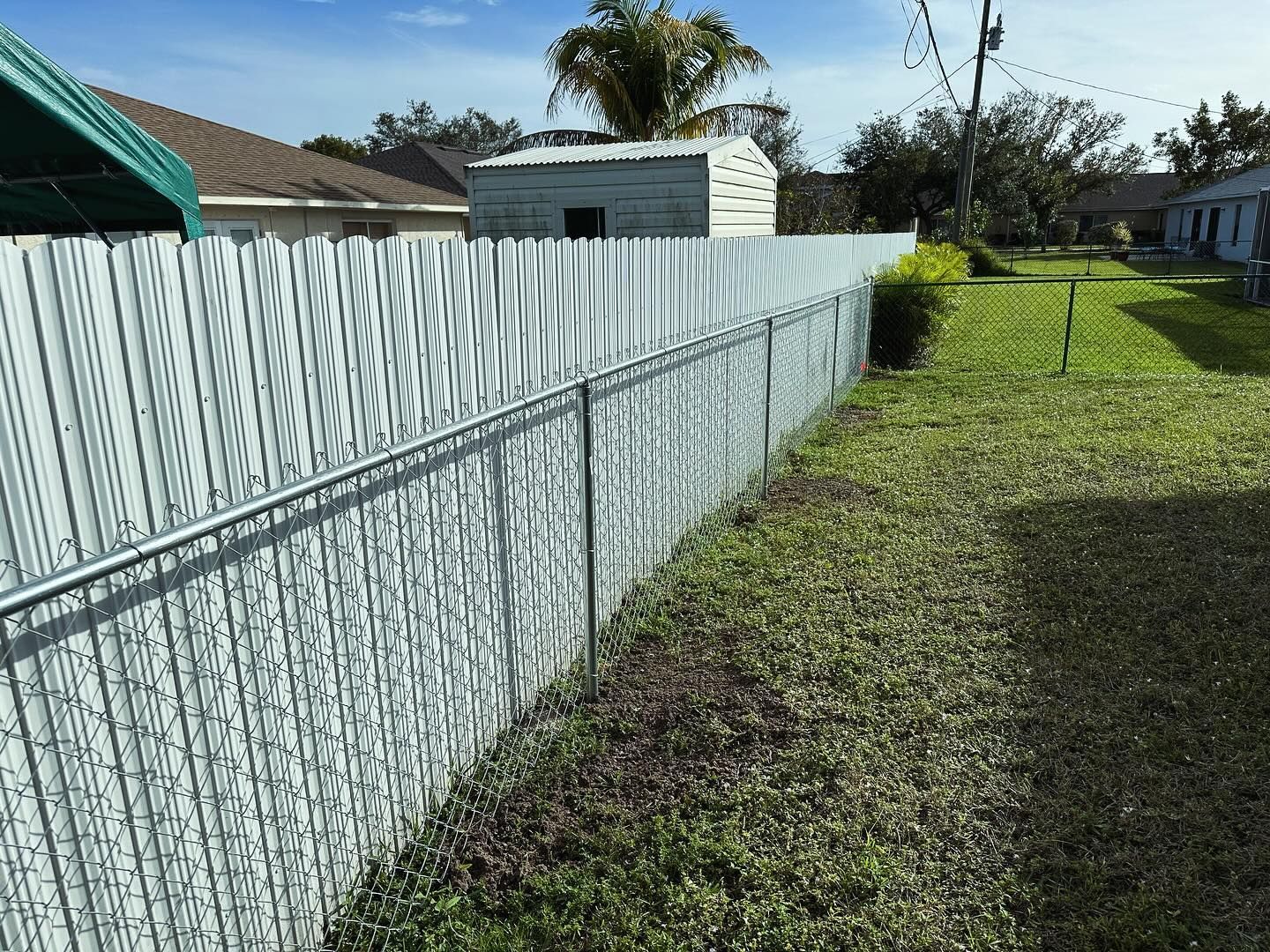 Chain link fence in a grassy backyard, separating properties. Gray fence with green grass.