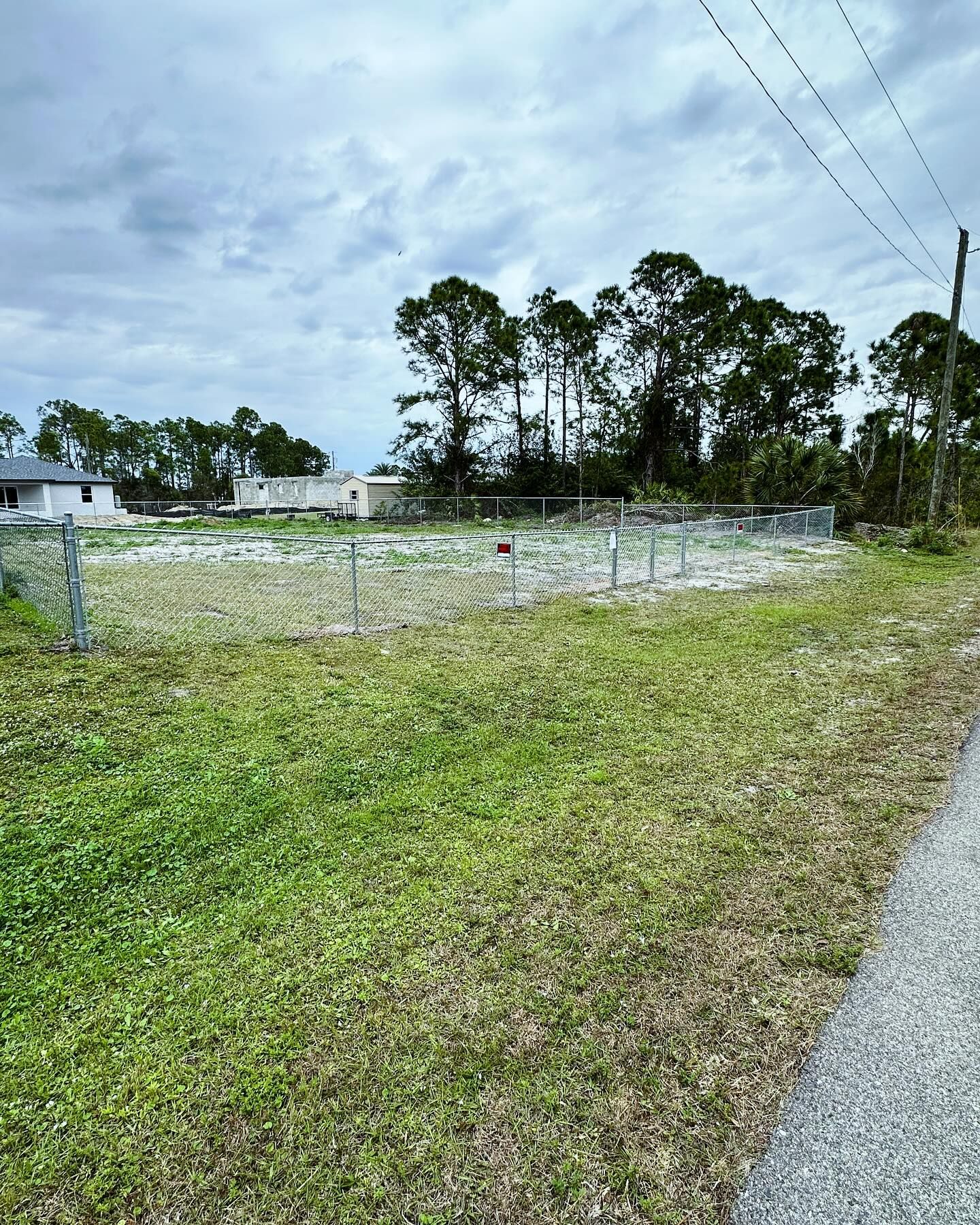 Grassy field with chain-link fence and trees under a cloudy sky.
