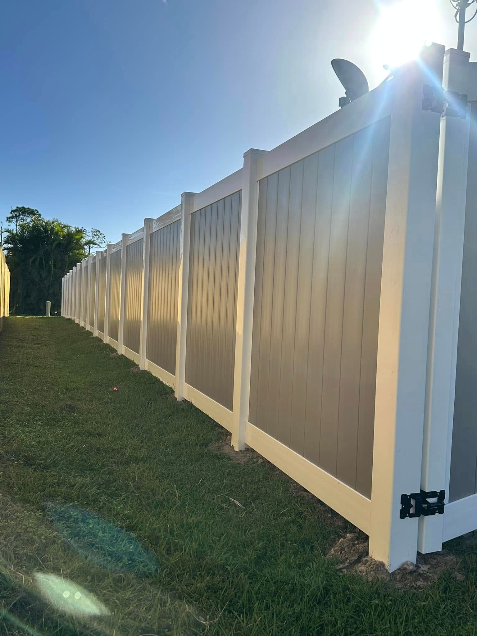 Long white and gray vinyl fence in yard with blue sky.