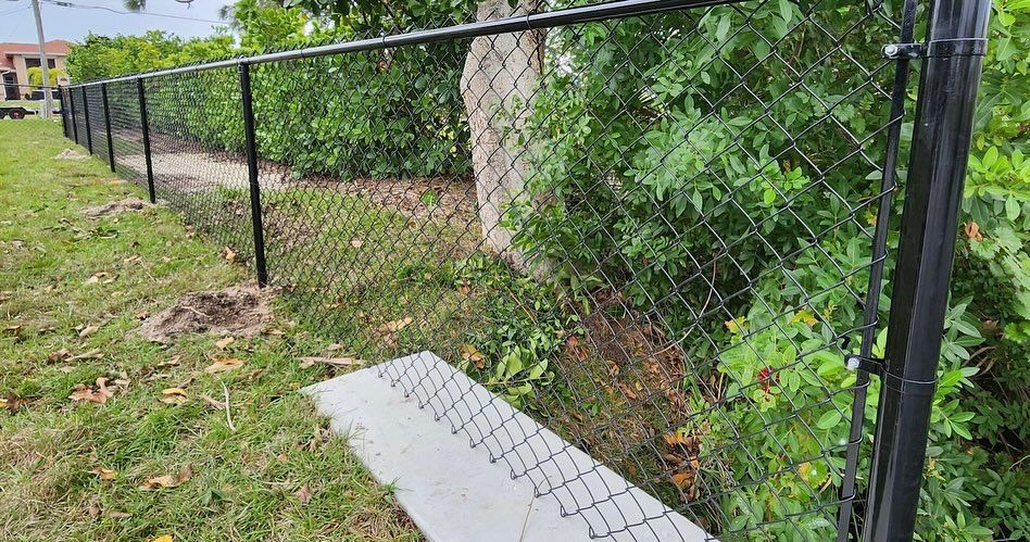 Black chain link fence along green grass, bushes, and a concrete barrier.