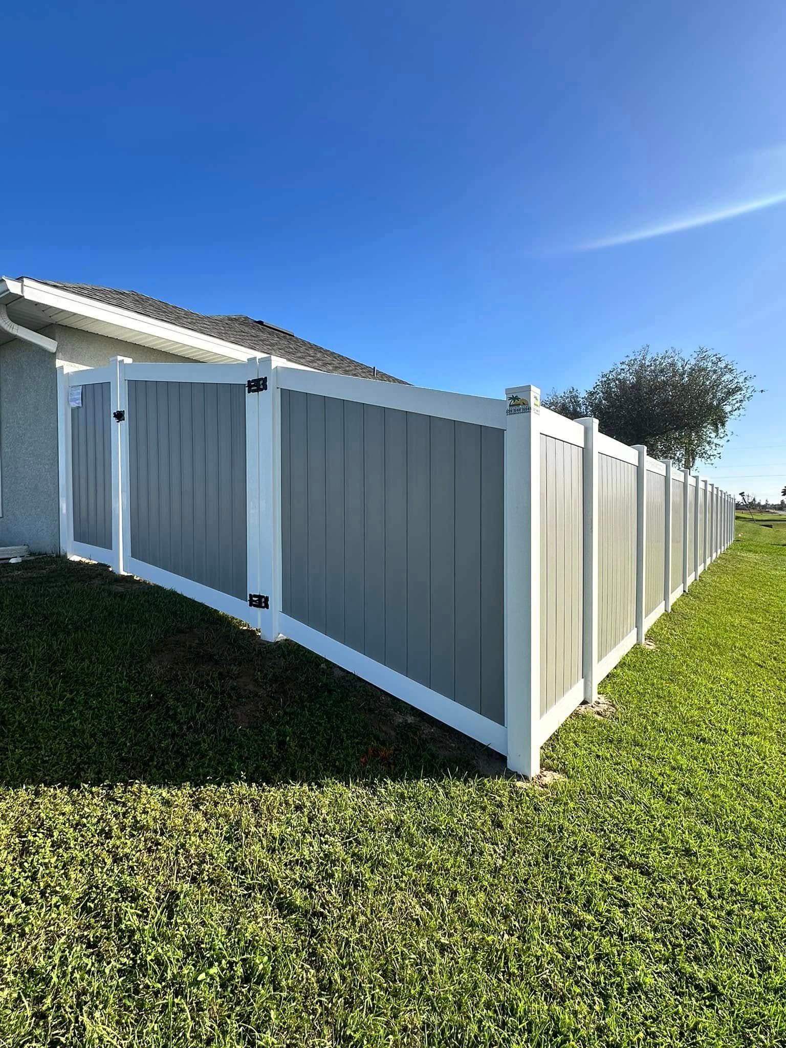 Gray and white privacy fence along a green lawn under a blue sky.