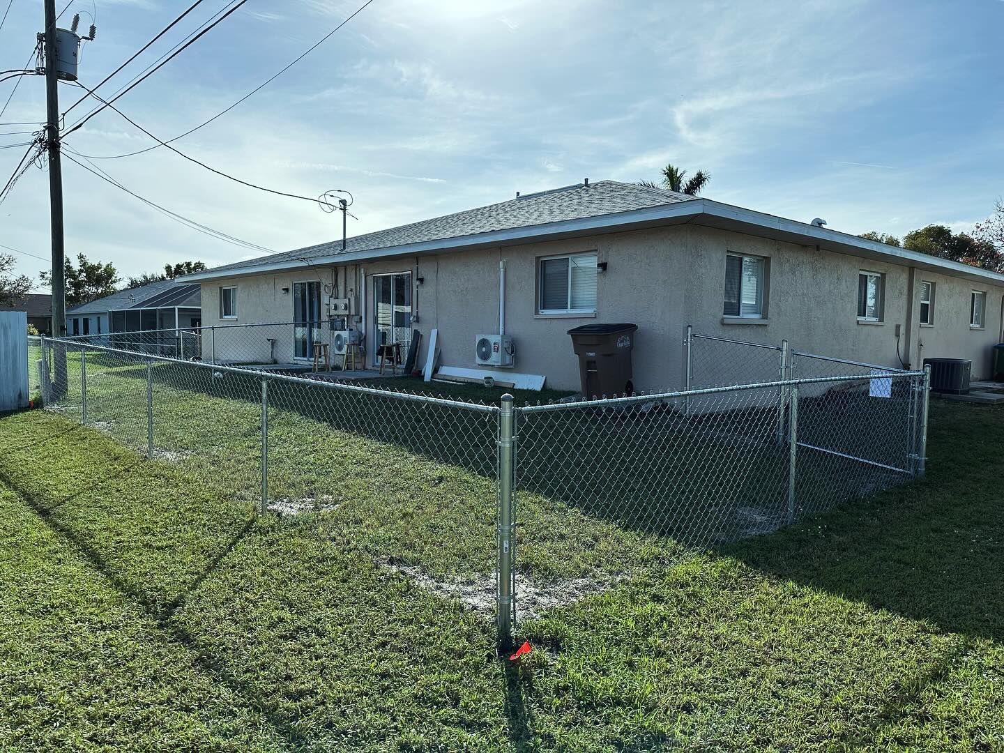 Low-angle view of a beige apartment building with a chain-link fence and green grass.