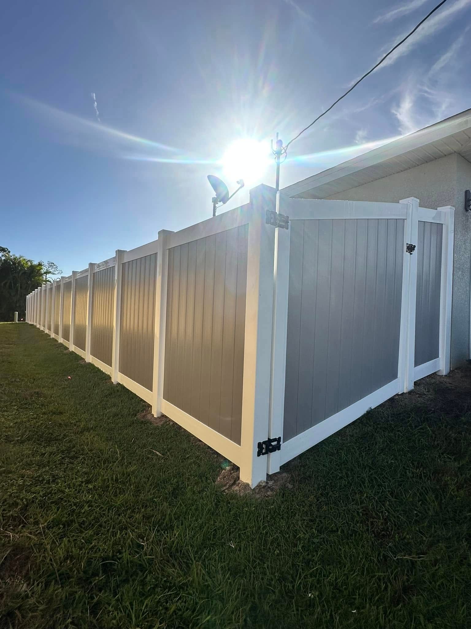 White and gray vinyl fence in front of a house on a sunny day.