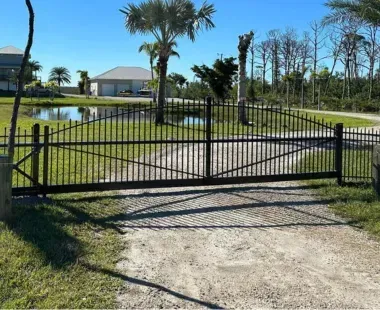 A black fence surrounds a dirt road leading to a house