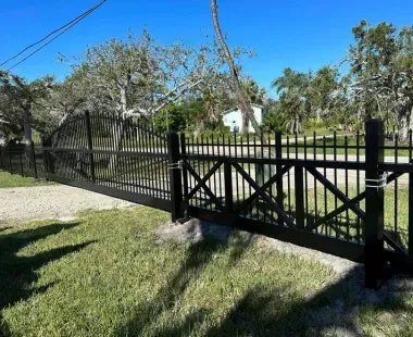 A black fence with a sliding gate is surrounded by grass and trees.