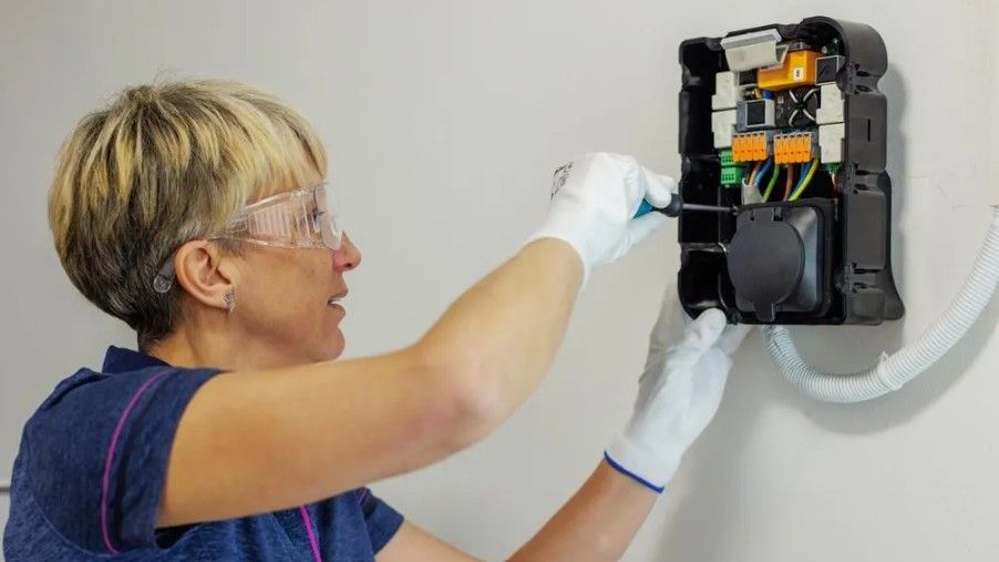 Technician in gloves inspecting wiring inside an open wall-mounted electrical panel.