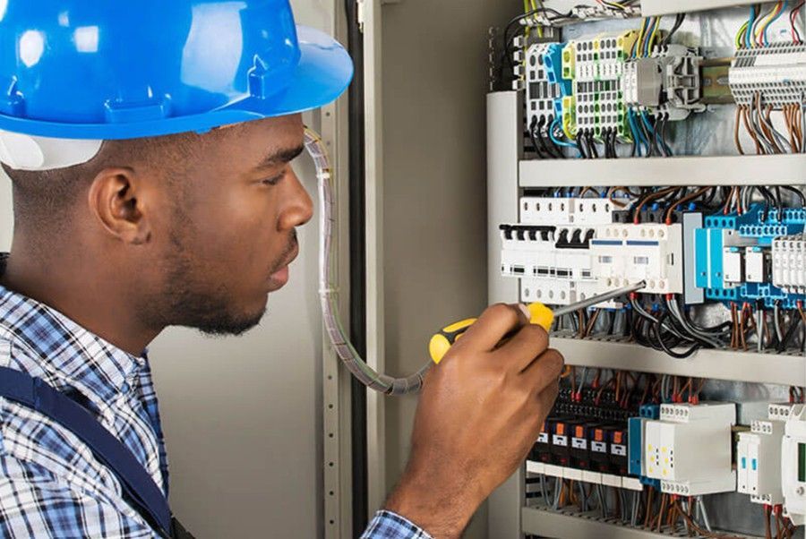 A person in a hard hat and plaid shirt installs a circular recessed light fixture into a ceiling under construction.