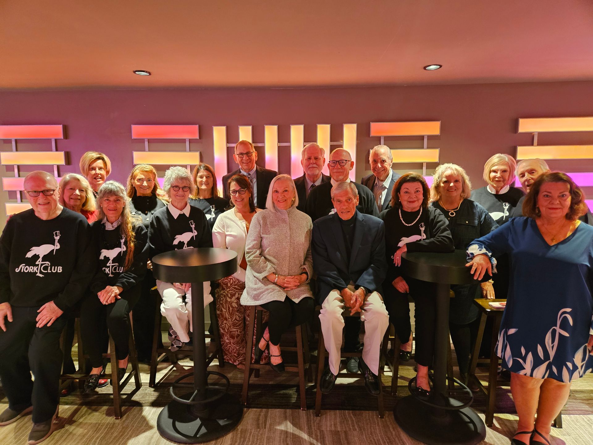 Group of people posing for a photo, some seated. They appear to be at an event, with smiles and formal attire.