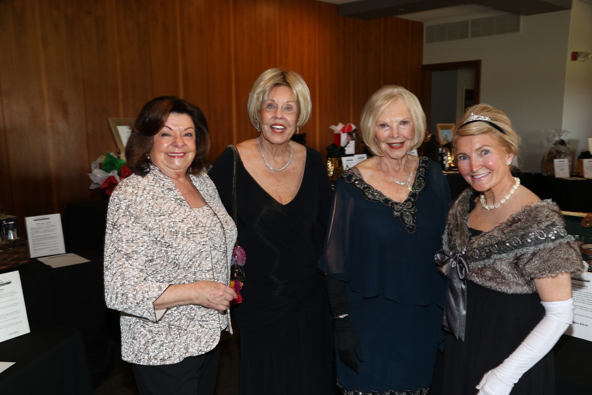 Four women in formal attire at an event, smiling, posing together indoors.