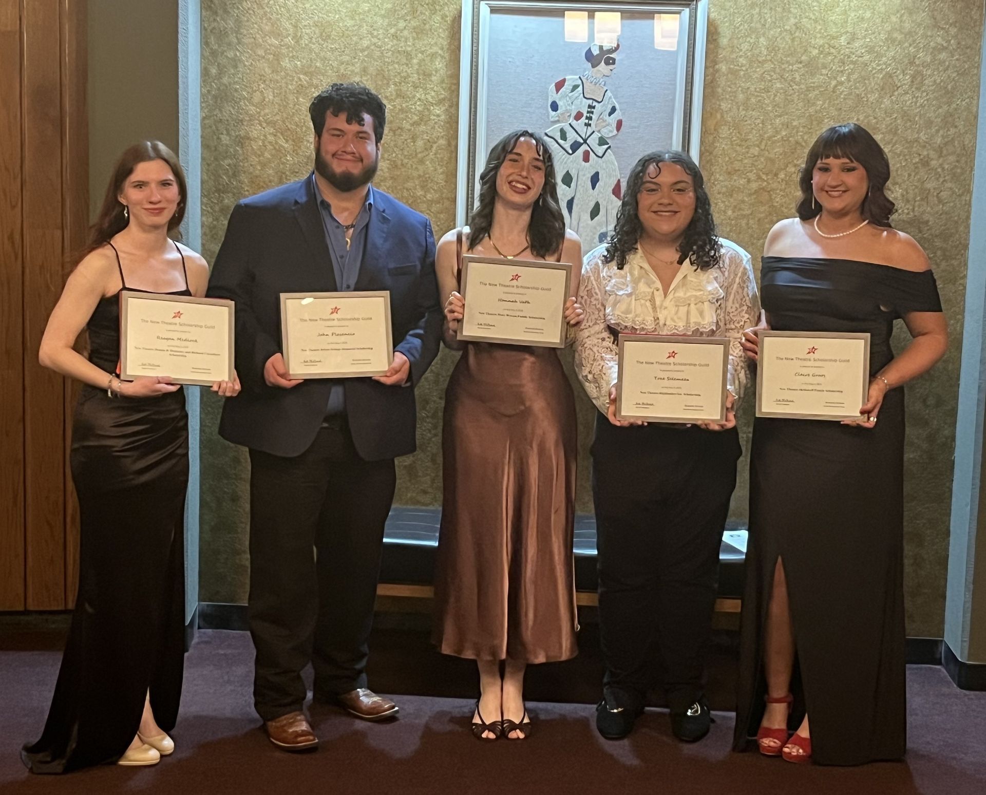 Five people holding certificates, smiling, in front of a decorated wall.
