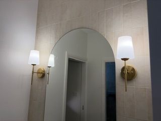 An arched mirror mounted on a tiled wall, flanked by two brass wall sconces — Channel Electrical In Swansea Heads, NSW