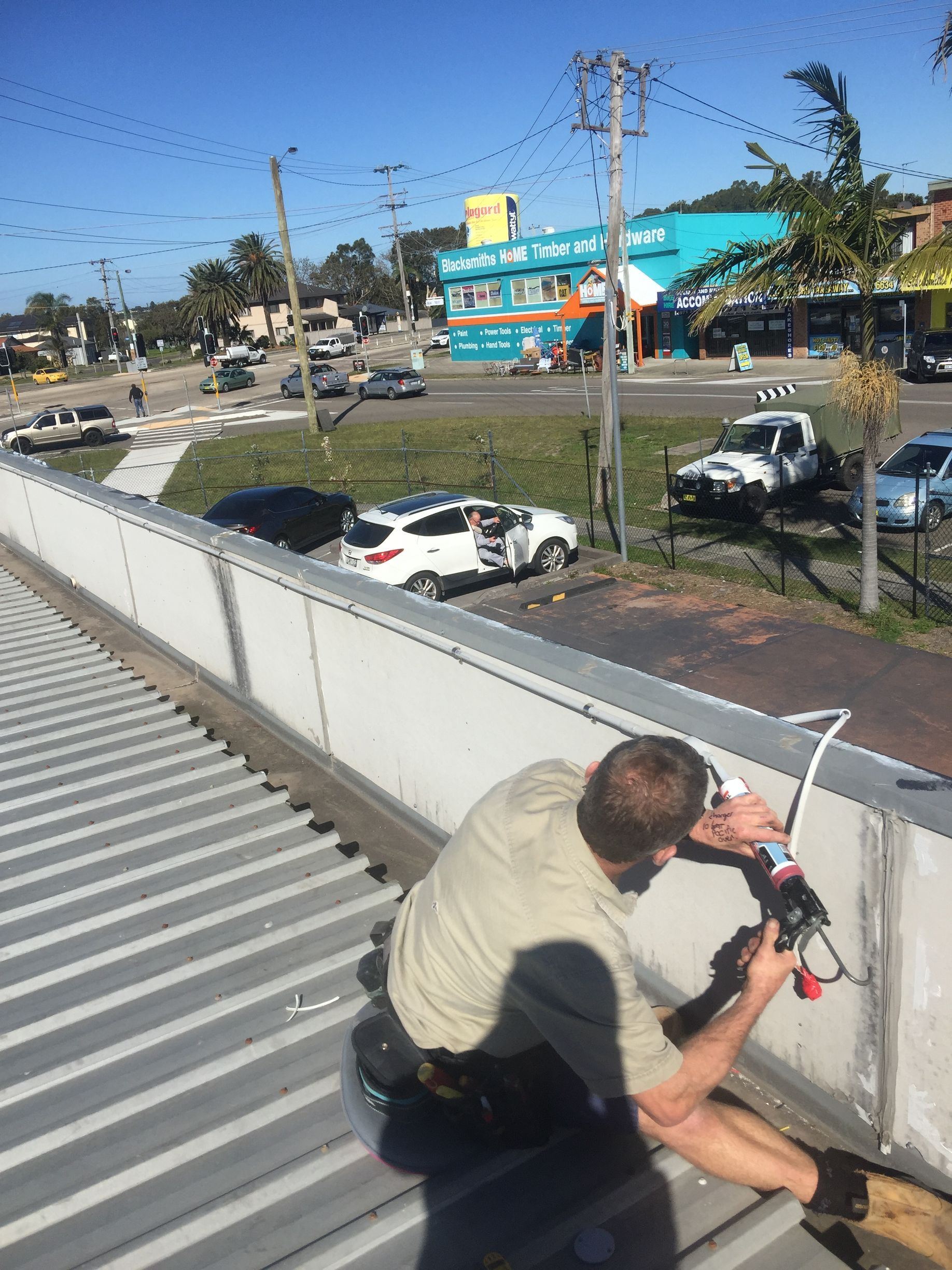 A person on a corrugated metal roof applies sealant to a concrete wall — Channel Electrical In Swansea Heads, NSW