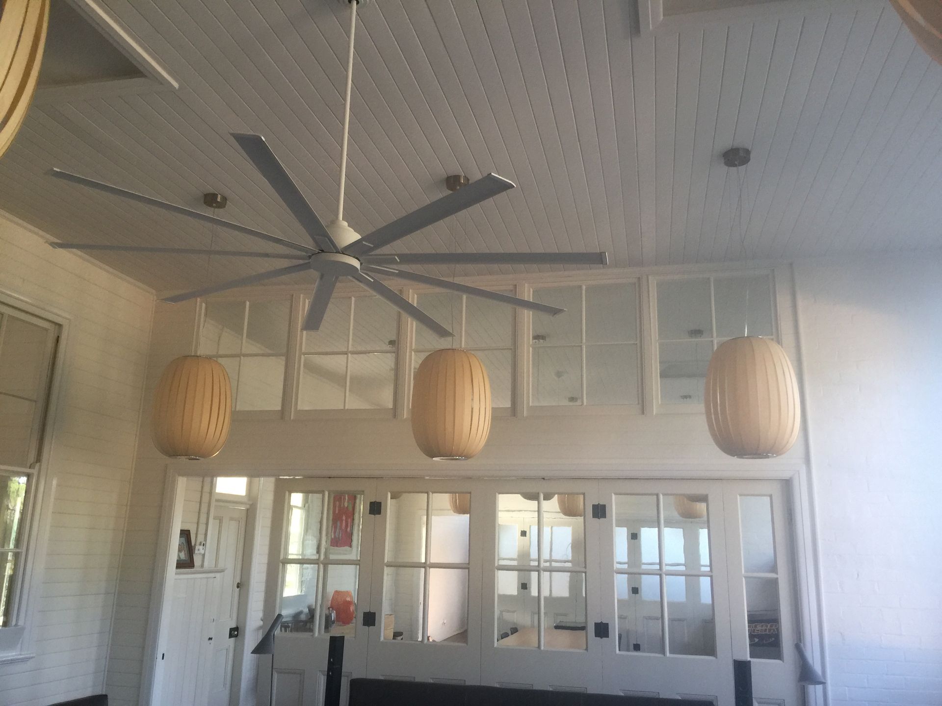 A large ceiling fan hangs in a room with white paneled walls — Channel Electrical In Swansea Heads, NSW