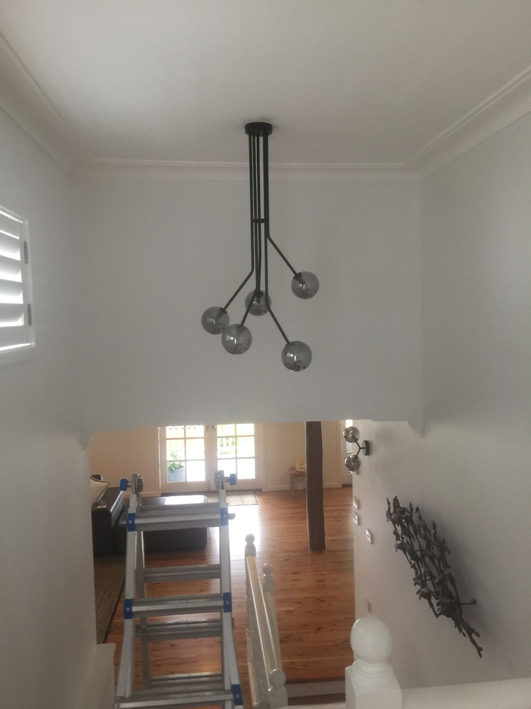 A modern multi-bulb pendant light hangs from a ceiling above a staircase — Channel Electrical In Swansea Heads, NSW