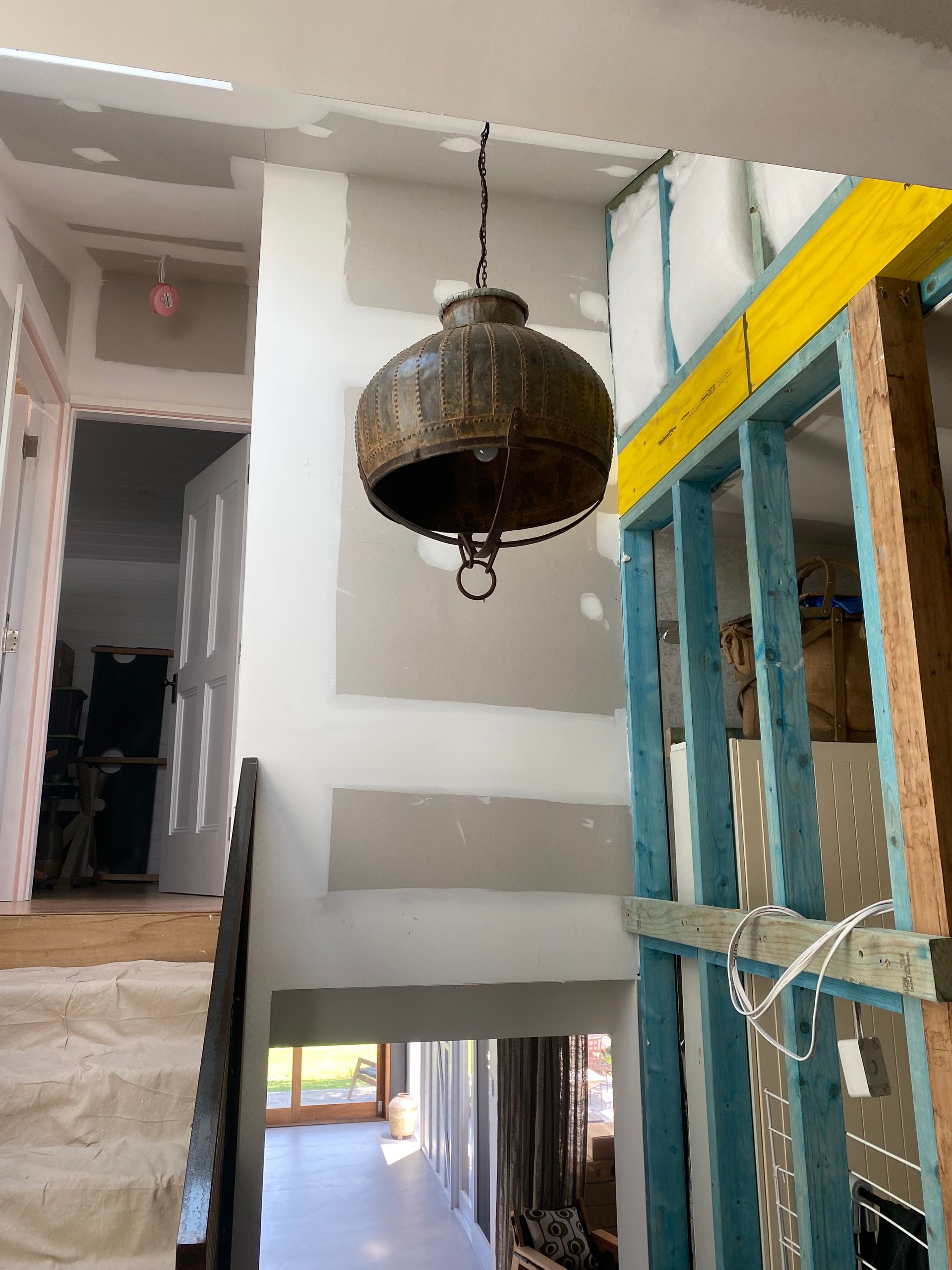 A large rustic metal pendant light hangs in a hallway under construction — Channel Electrical In Swansea Heads, NSW