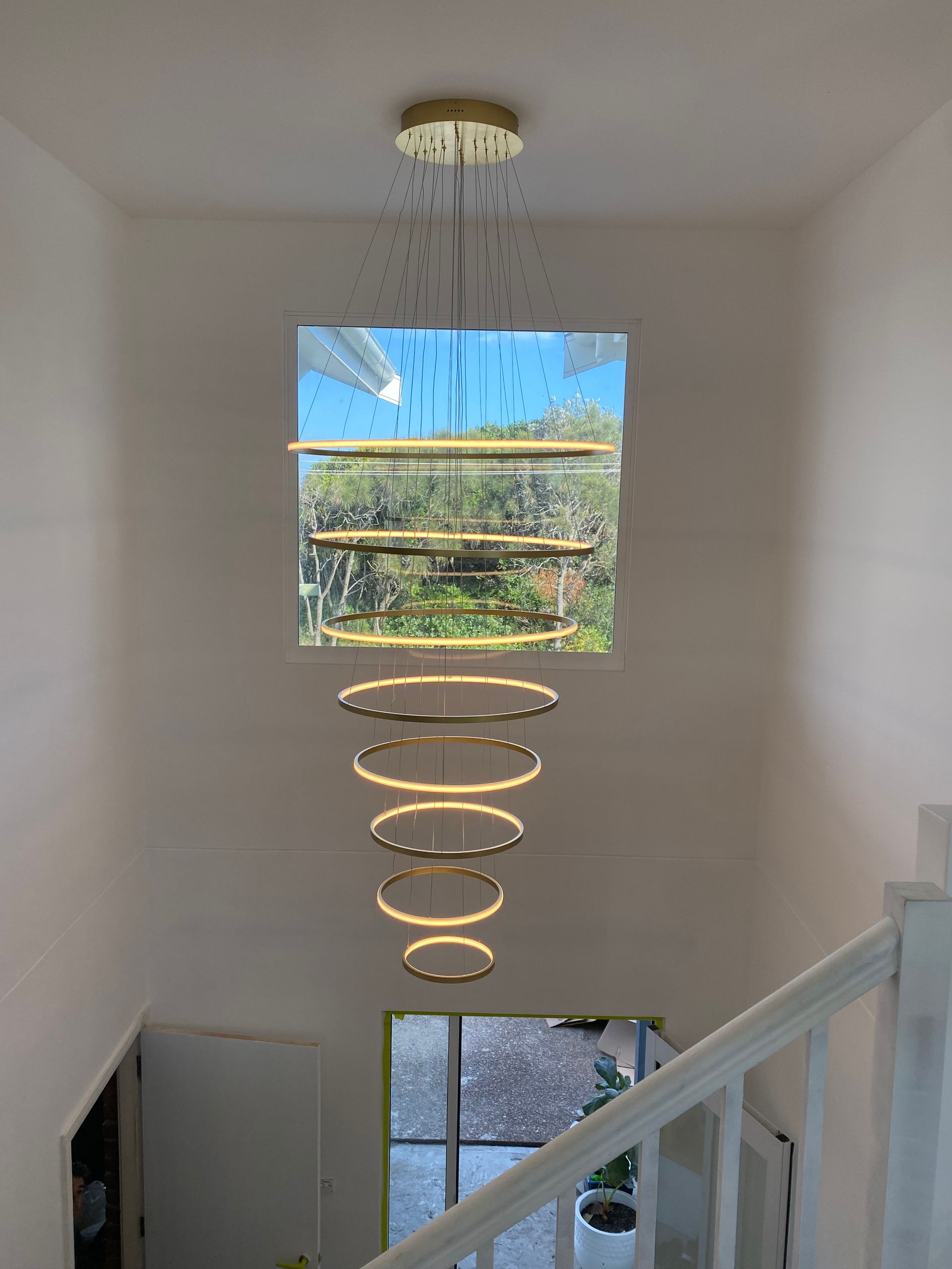 A tiered gold ring chandelier hanging in a tall stairwell — Channel Electrical In Swansea Heads, NSW