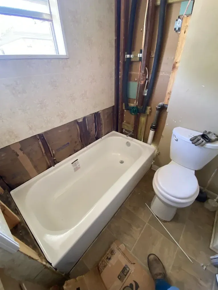 Bathroom renovation with a new bathtub and exposed walls. A toilet is visible to the right.