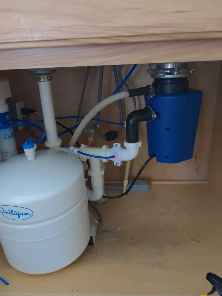 Under-sink cabinet with a water filtration system, garbage disposal, and plumbing.