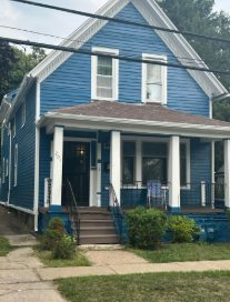 Blue two-story house with a white porch and trim, set on a green lawn.
