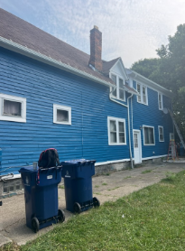Blue house with white trim, two blue trash cans in front.