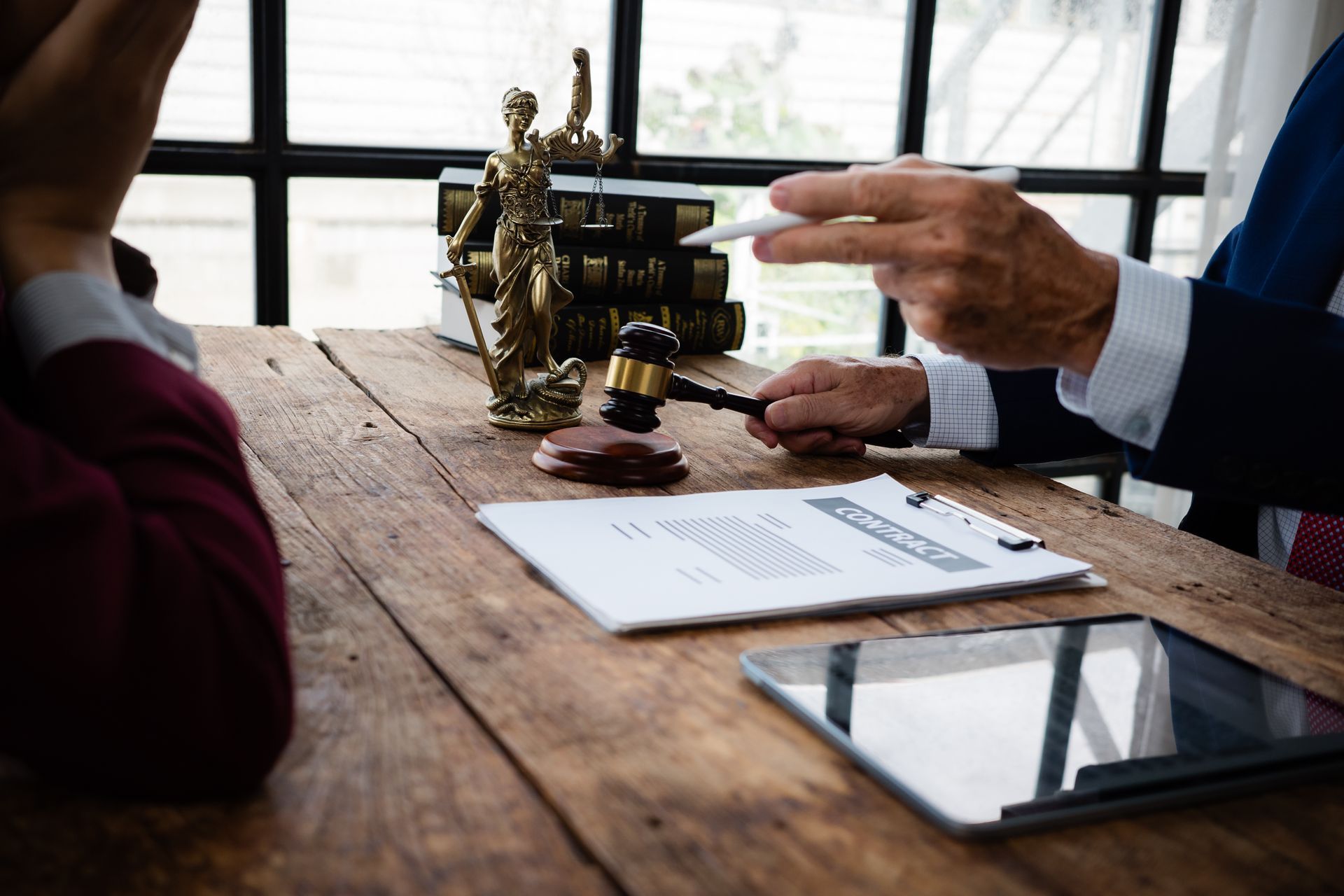 Lawyer and client meeting with legal documents, gavel, and tablet on office desk.
