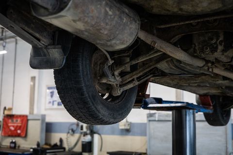 Underside of a car lifted in a repair shop; visible tire, exhaust, and suspension components.