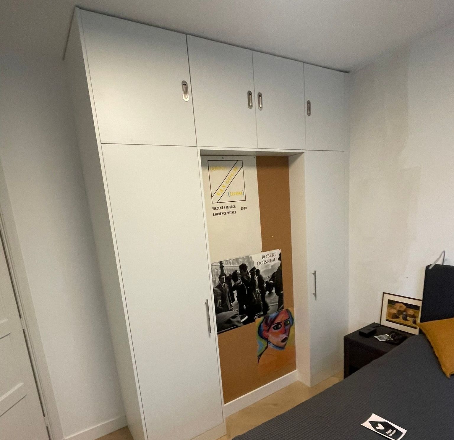 Een slaapkamer met witte maatwerk kasten en een prikbord aan de muur.