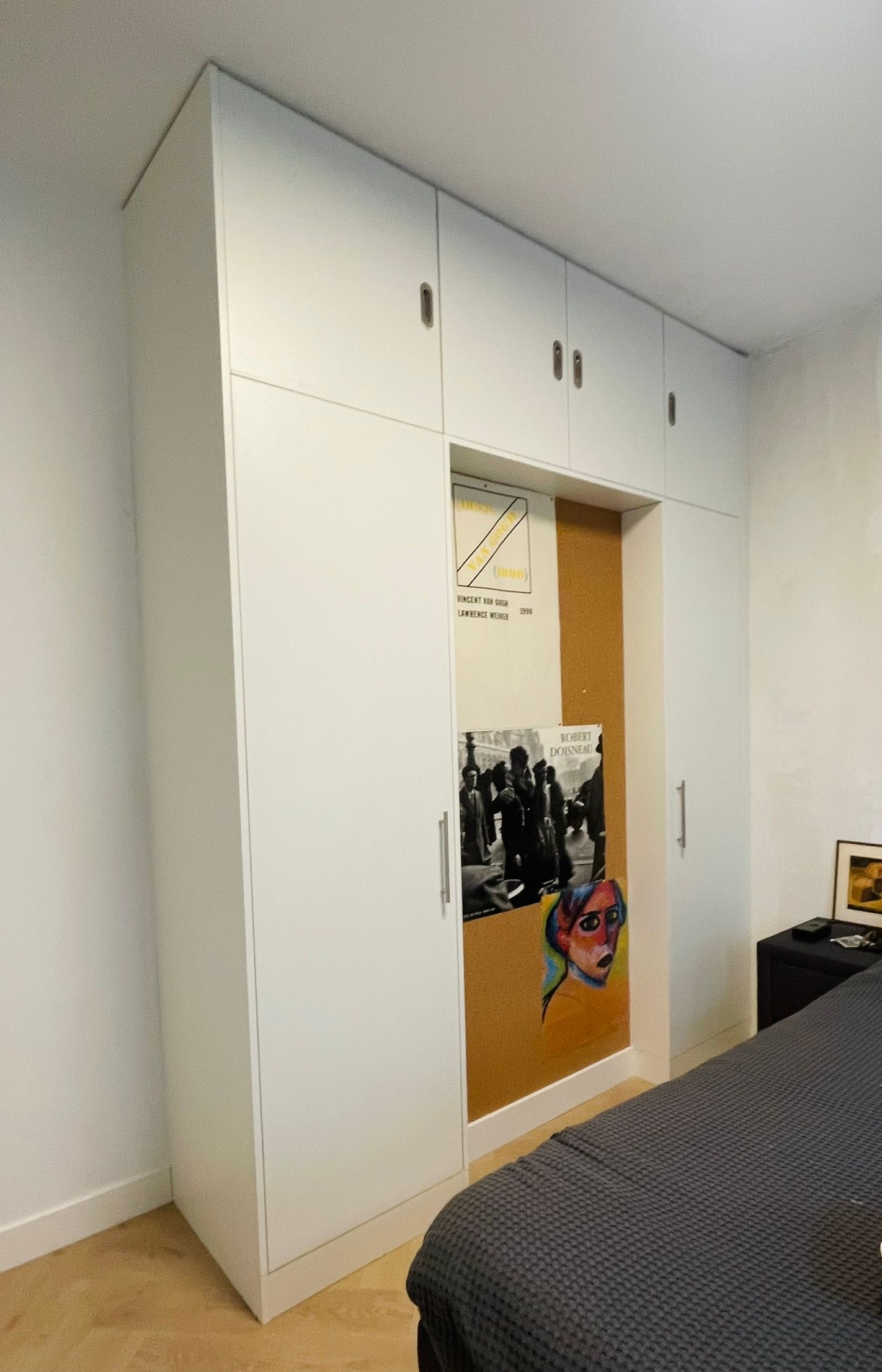 Een slaapkamer met witte maatwerk kasten en een prikbord aan de muur.