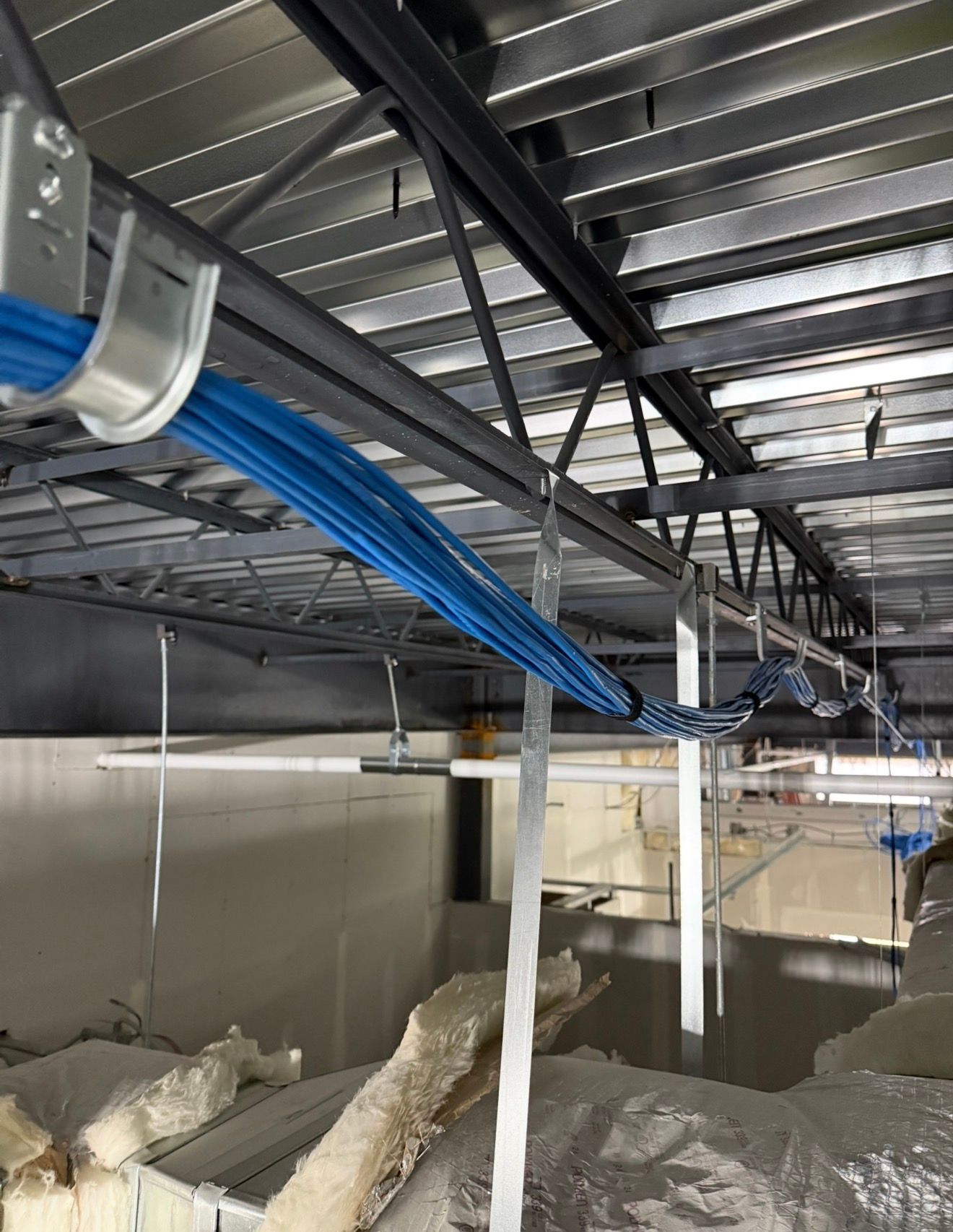 Industrial ceiling with blue cables and silver ducts above a partially built concrete interior.