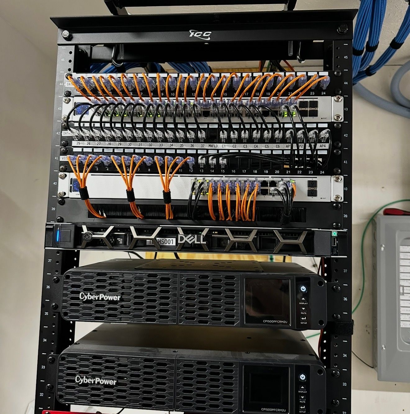 Network rack with patch panels, switches, and servers, with orange and black cables connected.