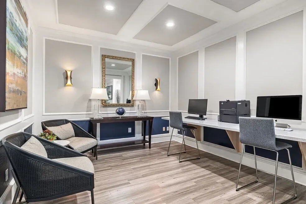 Business center with computers and a printer, seating area with chairs and a table, and decorative mirror.