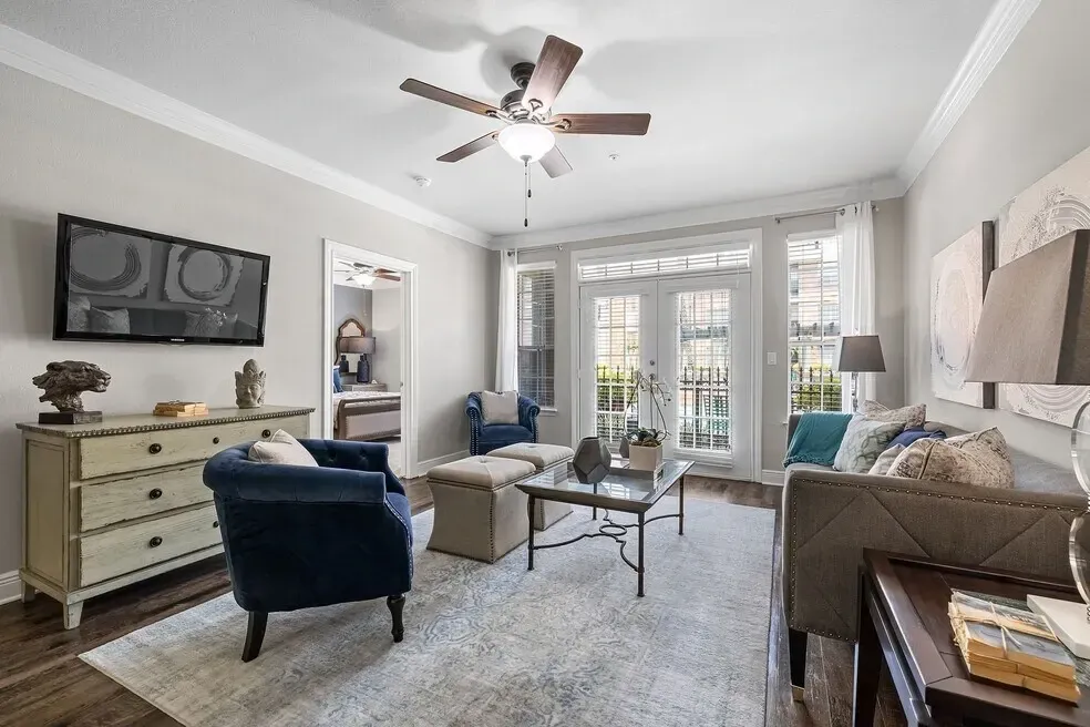 Living room with a sofa, chairs, coffee table, and TV. A doorway leads to a bedroom.